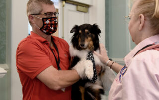 Man holds therapy dog in his arms while talking to an ATD volunteer.