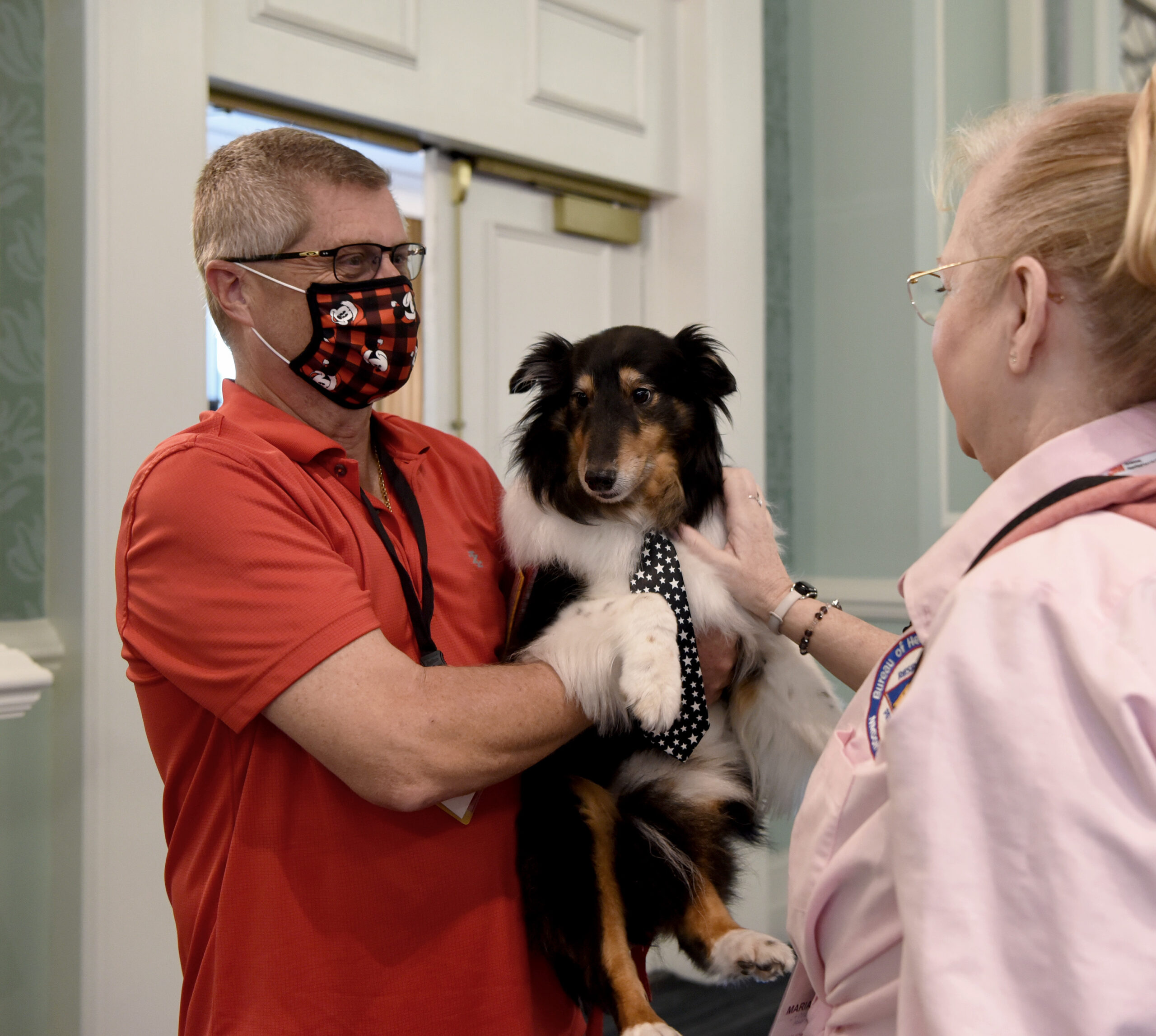Man holds therapy dog in his arms while talking to an ATD volunteer.