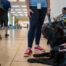 A black lab lays down in an airport staring up at someone off camera.