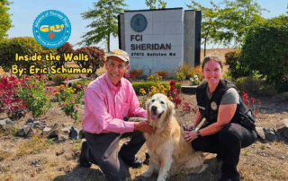 A man and woman kneel next to a golden retriever in front of a Federal Corrections Institution sign.
