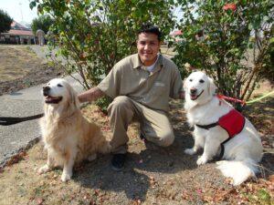 A prisoner kneels with two golden retrievers smiling.